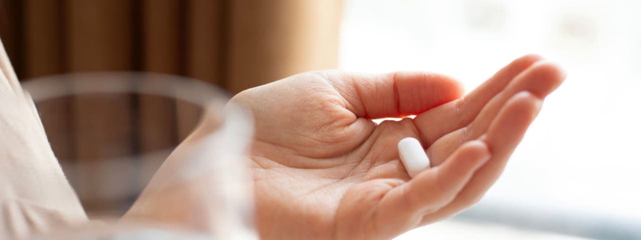 A woman's hand holding a medication tablet while her other hand holds a glass of water